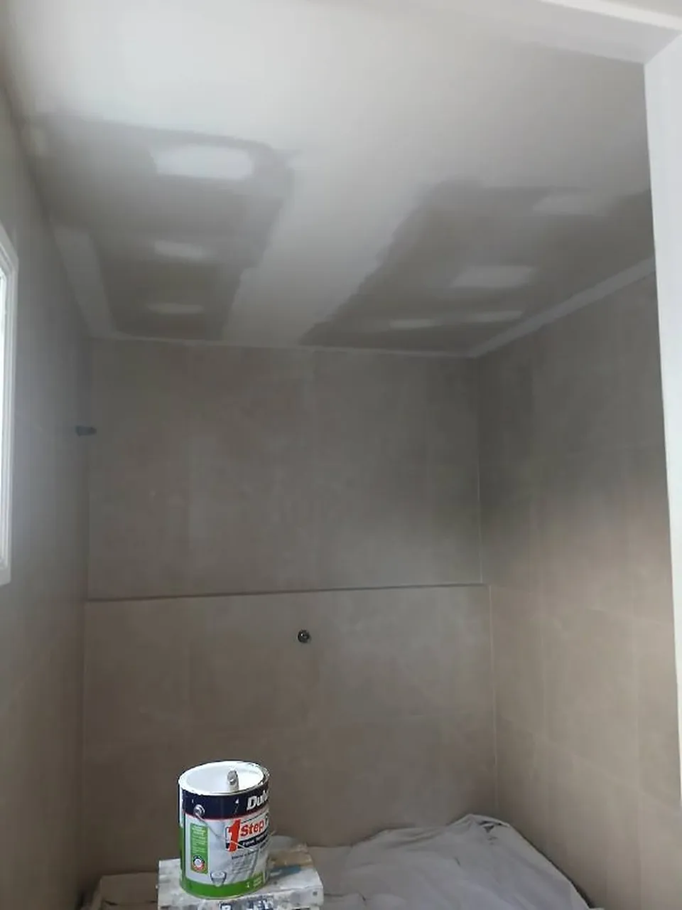 Bathroom ceiling with sanded patches and a tin of paint on a drop sheet
